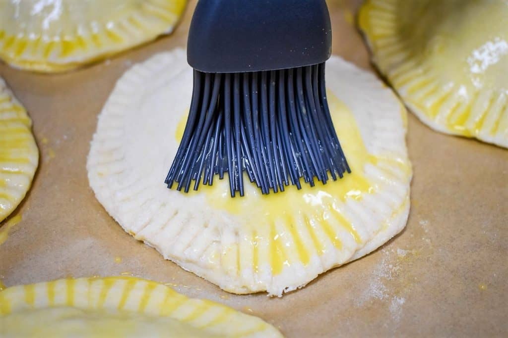 A dark gray silicone pastry brush brushing an egg wash on a biscuit.