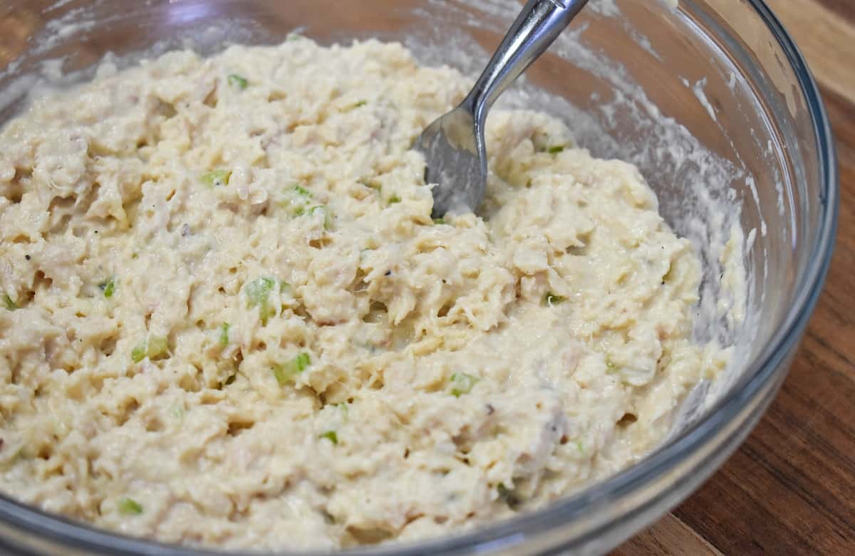 The tuna salad after being stirred with a fork in a large clear bowl.