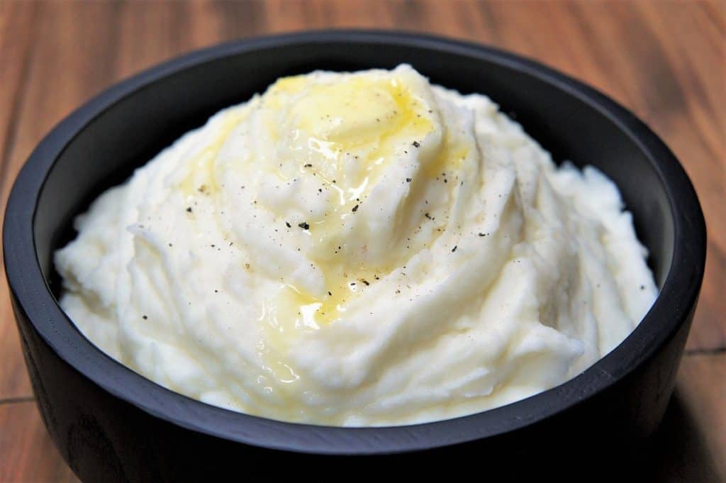 Mashed Potatoes with melted butter on top served in a black serving bowl