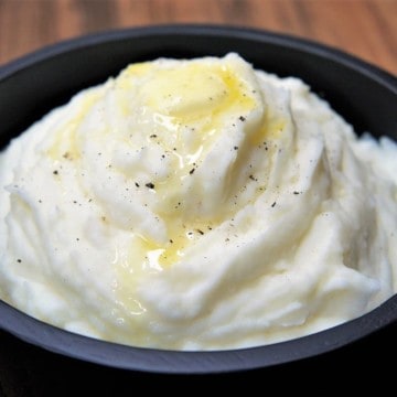 Mashed Potatoes with melted butter on top served in a black serving bowl