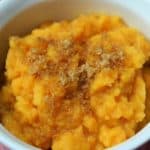 Mashed Sweet Potatoes, topped with brown sugar and served in a white ramekin on a red cloth