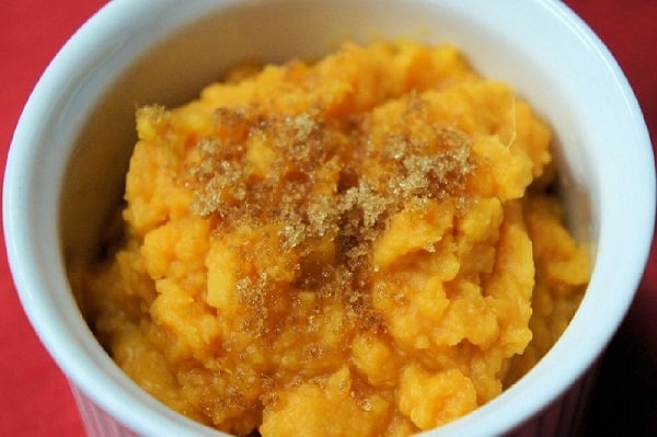 Mashed Sweet Potatoes, topped with brown sugar and served in a white ramekin on a red cloth