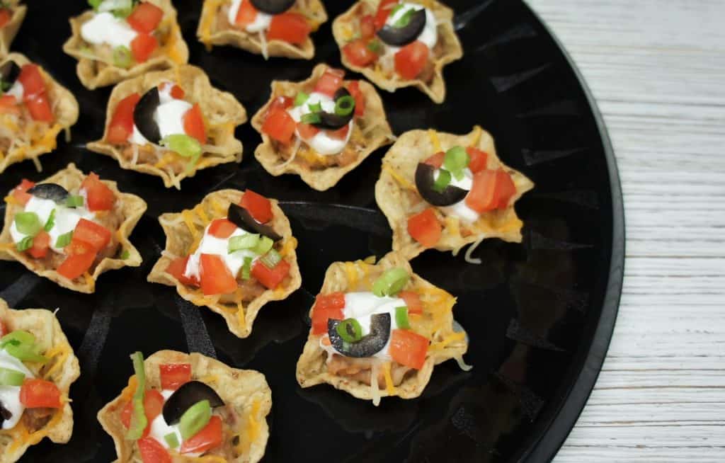 A top picture of mini taco bites arranged on a round, black serving tray.