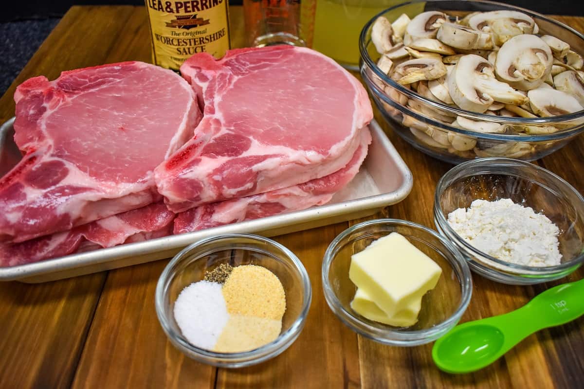 The ingredients for the mushroom pork chops recipe, prior to cooking, displayed on a wood cutting board.