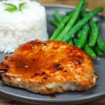 The orange glazed pork chop served on a gray plate with white rice and green beans.