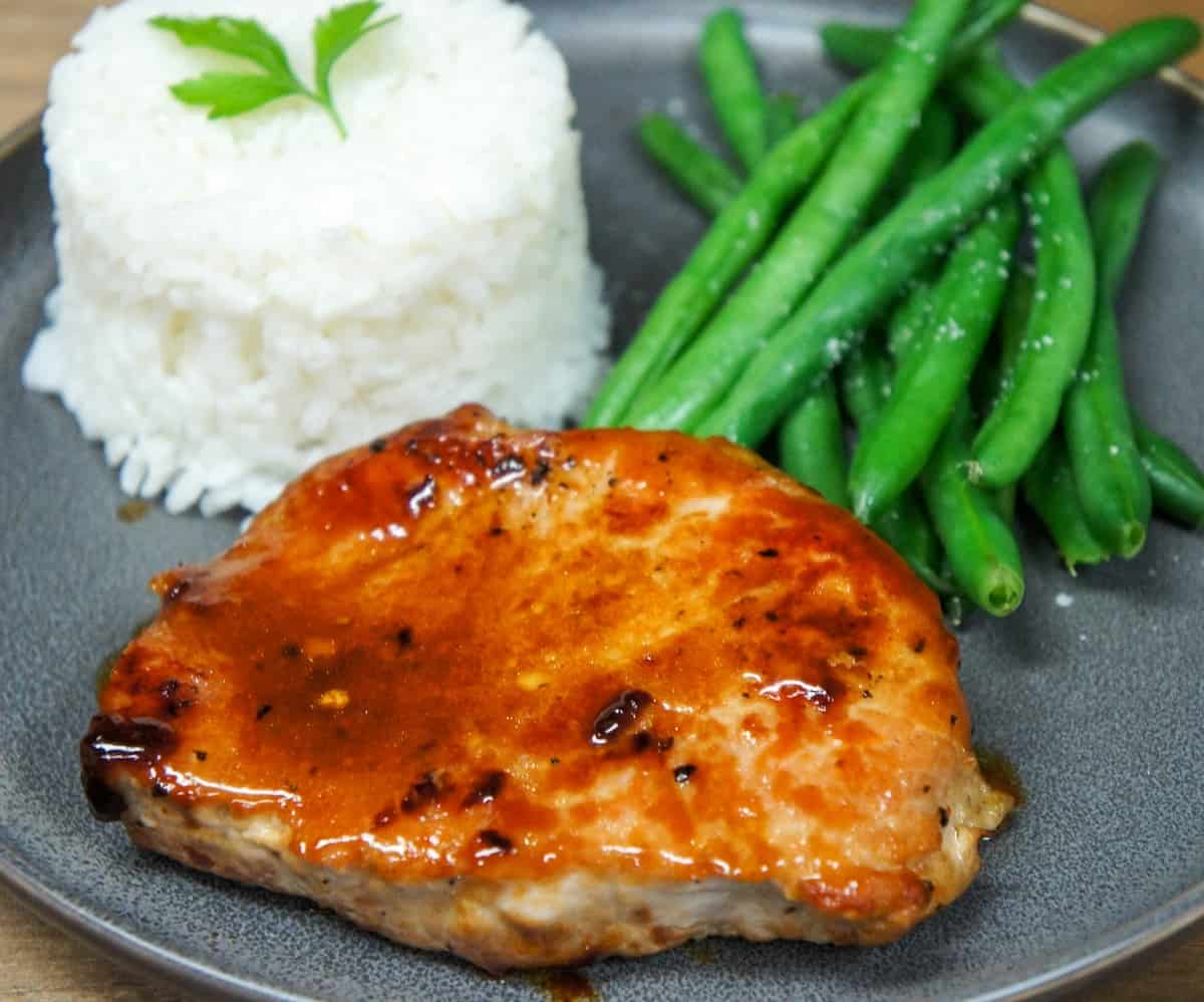 The pork chop served with white rice and green beans on a gray plate.