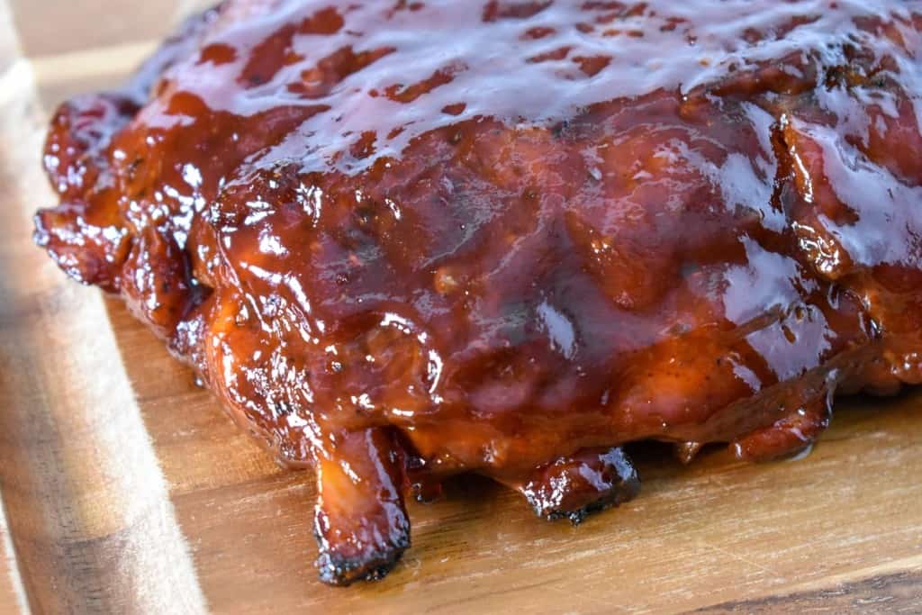 An image of the baked barbecue ribs before slicing set on a wood cutting board.