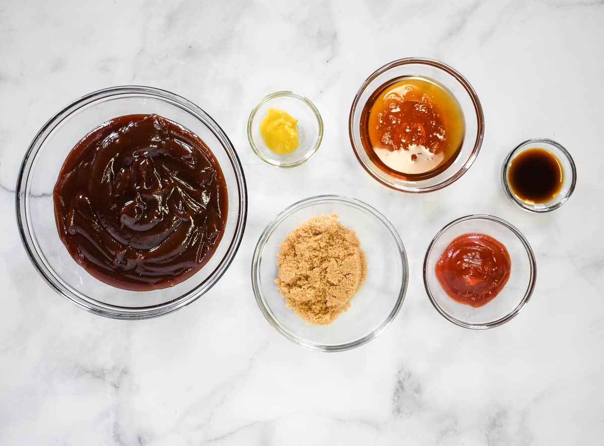 The ingredients for the rub and the sauce separated in clear bowls and arranged on a white table.