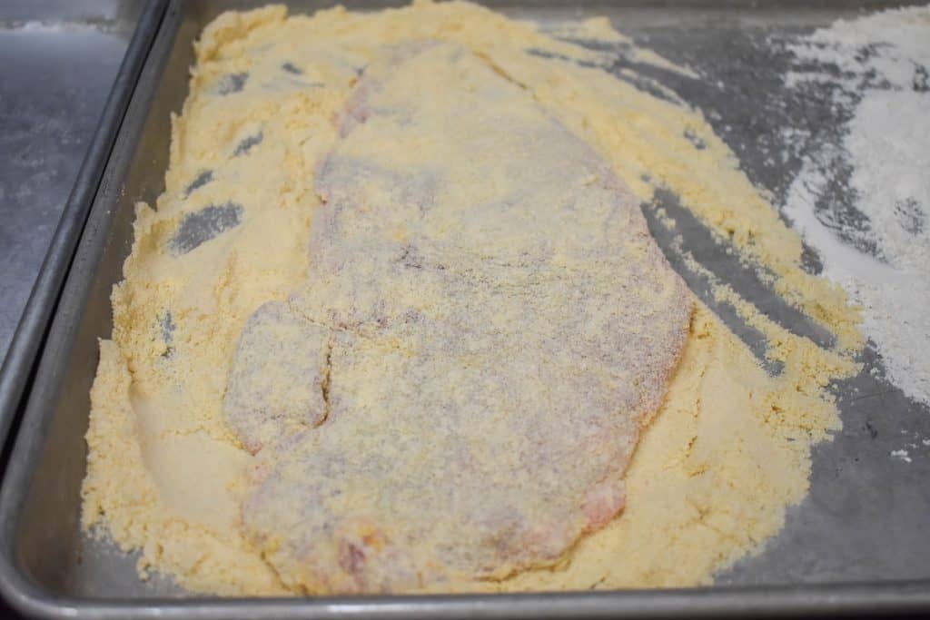 A large, thin steak coated in cracker meal on a metal baking sheet.