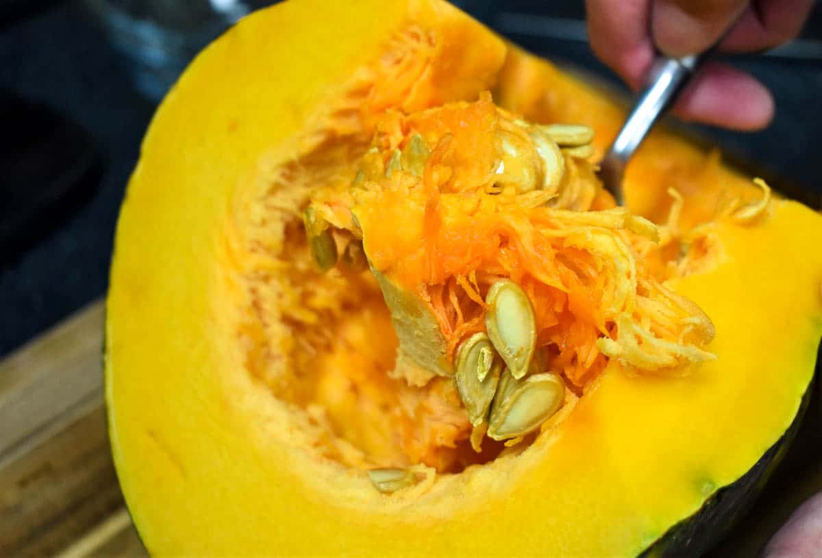 A close up image of a cut pumpkin with a spoon being used to scoop out the stringy flesh and seeds.