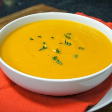 The creamy pumpkin soup served in a large white bowl set on an orange linen on a large white plate.