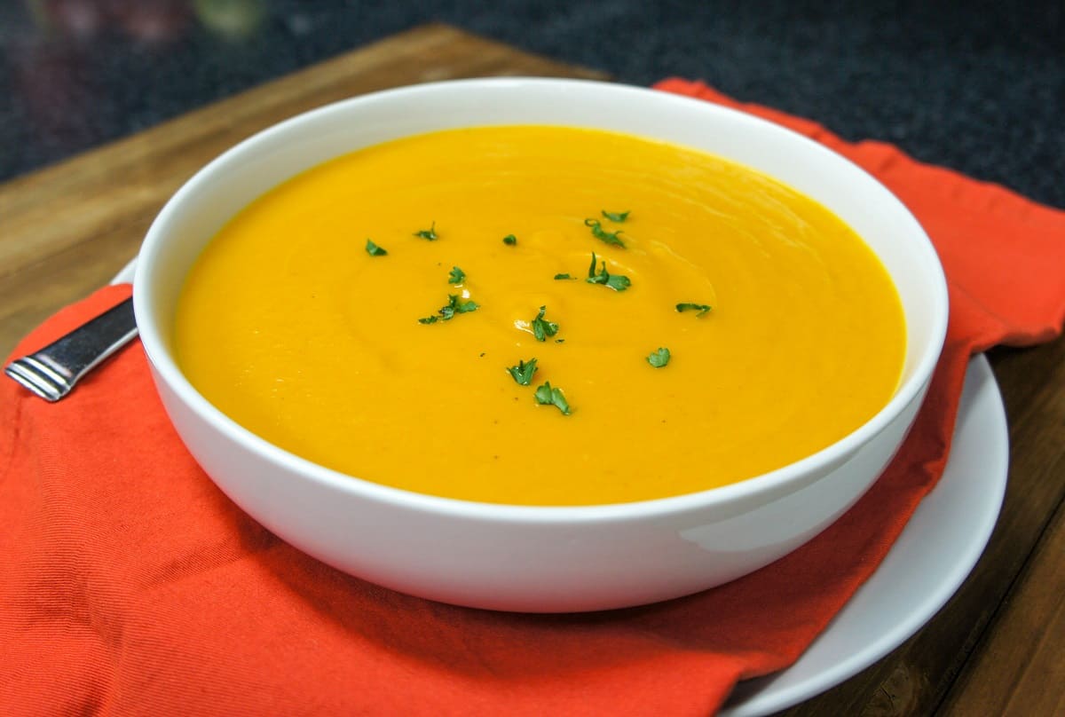 The creamy pumpkin soup served in a large white bowl set on an orange linen on a large white plate.