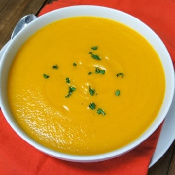 A top shot of the soup in a large white bowl set on an orange linen on a white plate with a spoon to the left.