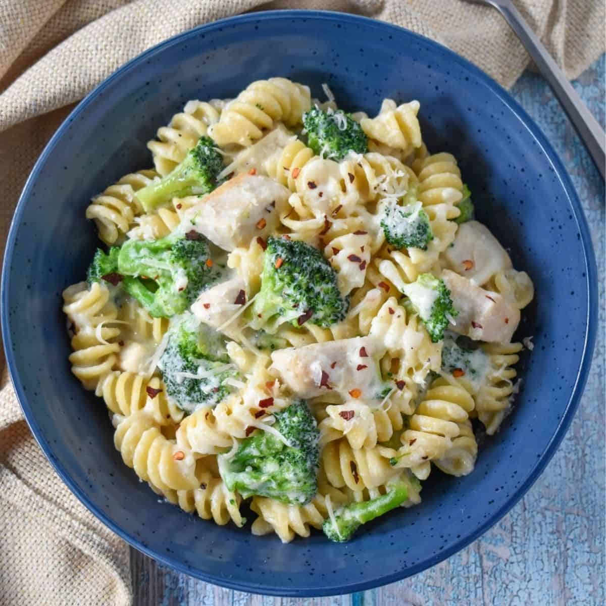 The pasta served in a blue bowl with a beige linen on the left side and displayed on a light aqua blue table.