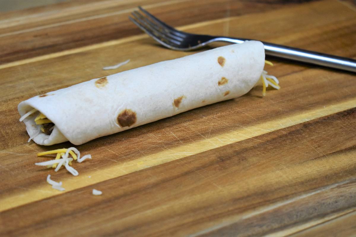 a rolled taquito on a wood cutting board.