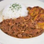Ropa Vieja served with white rice and fried sweet plantains served on a white plate.