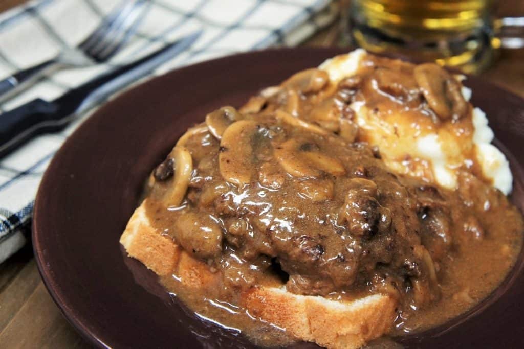 Salisbury Steak Open-Face Sandwich served with a side of mashed potatoes and covered with mushroom gravy on a brown plate