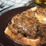 Salisbury Steak Open-Face Sandwich served with a side of mashed potatoes and covered with mushroom gravy on a brown plate