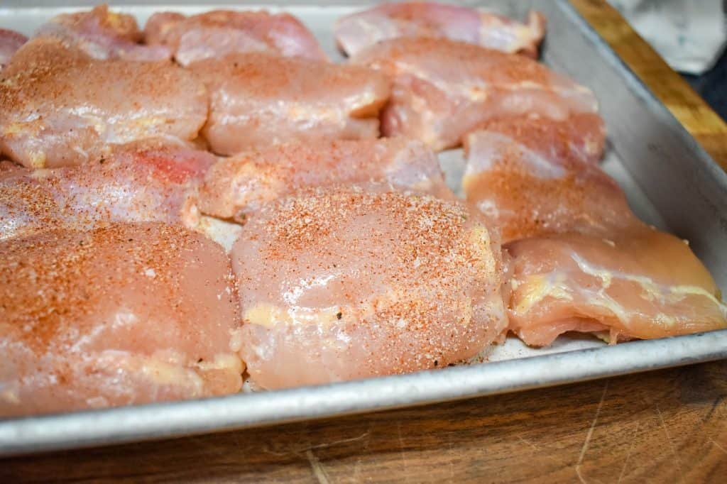 Seasoned raw chicken thighs arranged on a metal sheet pan.