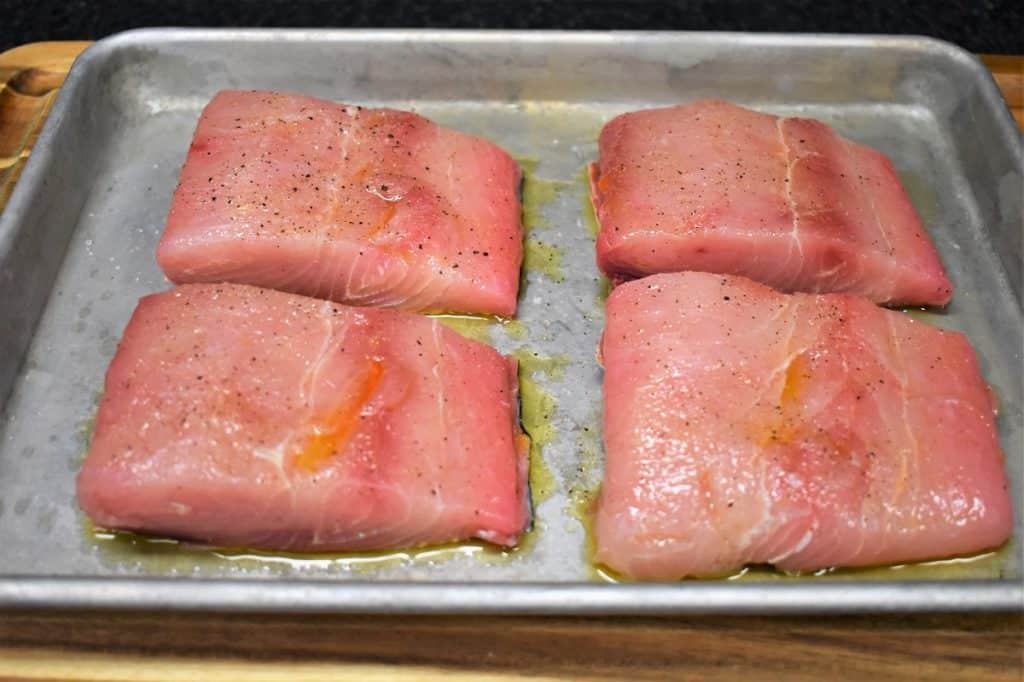 Four seasoned mahi mahi fillets on a baking sheet.