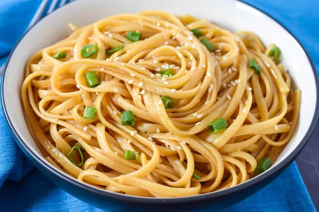 Sesame Noodles Served in a black bowl with a white interior on a blue linen.