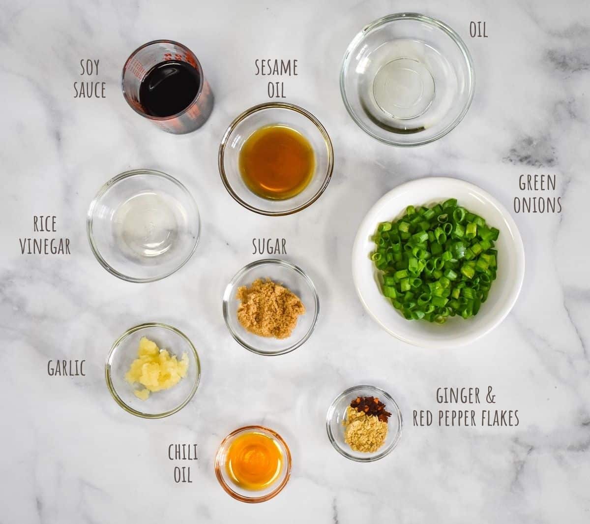 The ingredients for the sesame sauce arranged on a white tables in glass bowls. The image has the name of the ingredient in small letters next to each.