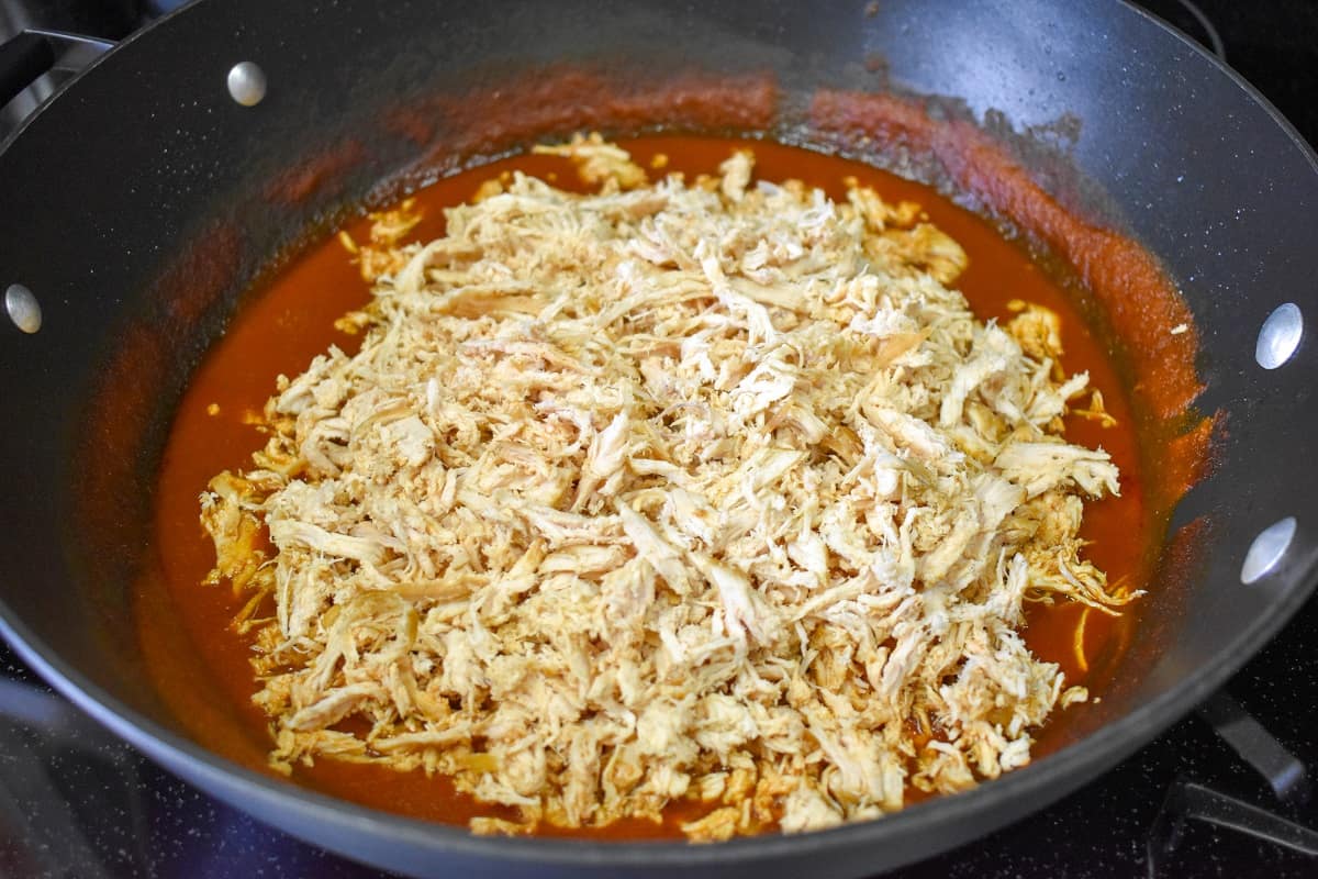 The shredded chicken added back to the sauce in a large, black skillet.