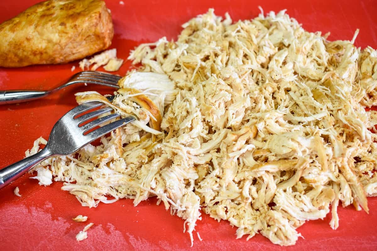 The cooked shredded chicken breast on a red cutting board with two forks.