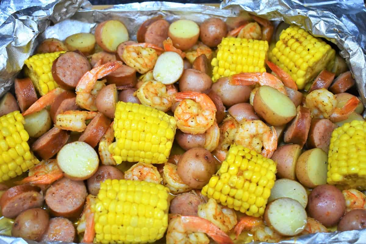 Sausage, shrimp, corn and potatoes in an open aluminum foil pack.