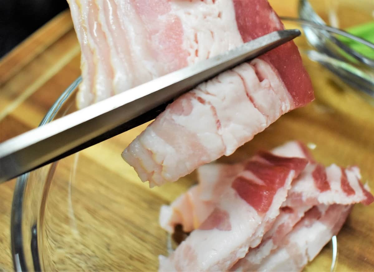 A close up image of scissors snipping bacon into roughly one inch pieces.