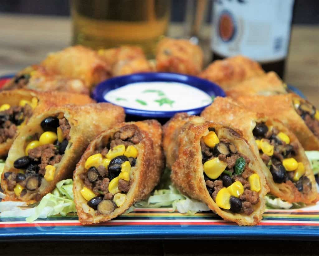 Southwestern egg rolls cut in half and arranged on a plate with a sour cream dipping sauce in the center.