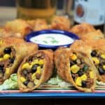 Southwestern egg rolls cut in half and arranged on a plate with a sour cream dipping sauce in the center.