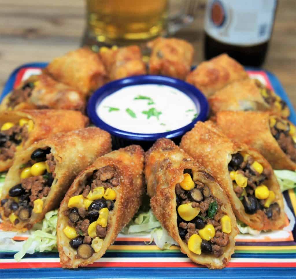 Southwestern egg rolls, cut in half and arranged on a platter with sour cream for dipping.