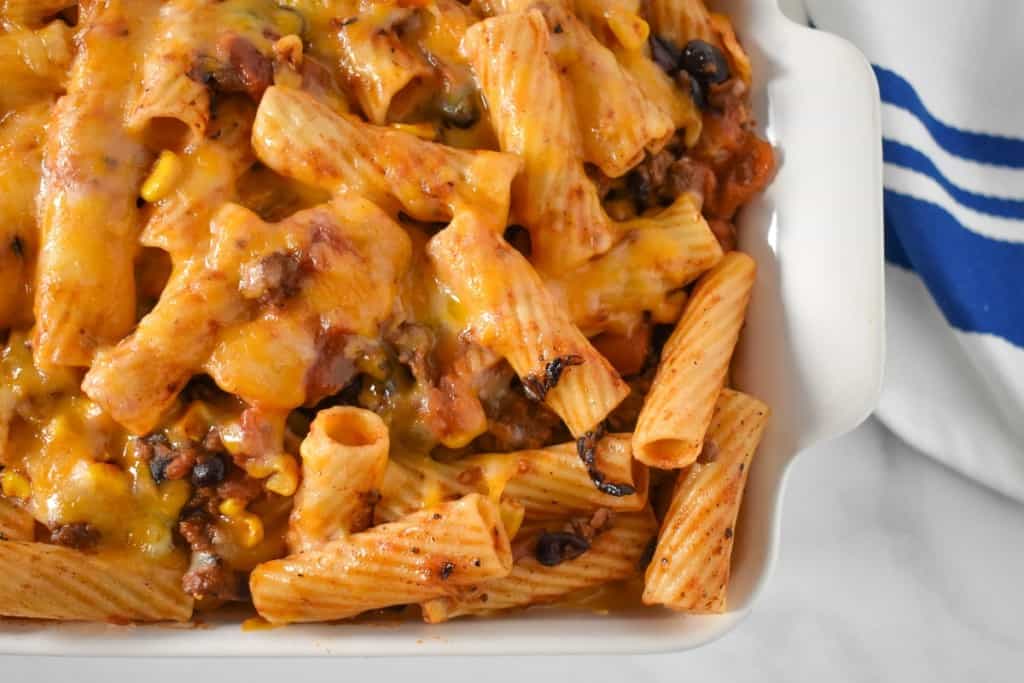 An image of the baked southwestern pasta in a white casserole dish with a blue and white kitchen towel.