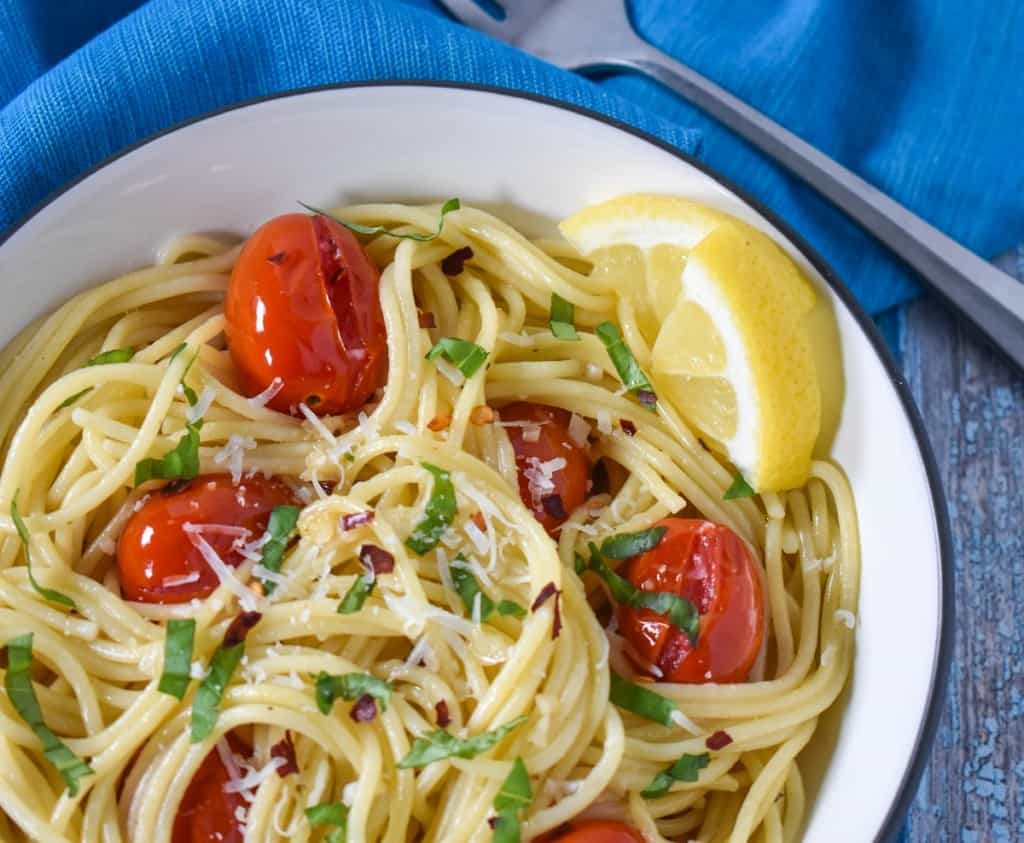 A close up image of the finished pasta dish served in a white bowl with a black rim with an aqua linen.