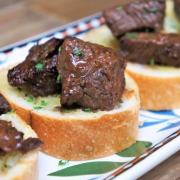 Cubes of sirloin steak on small toast rounds arranged on a colorful platter.