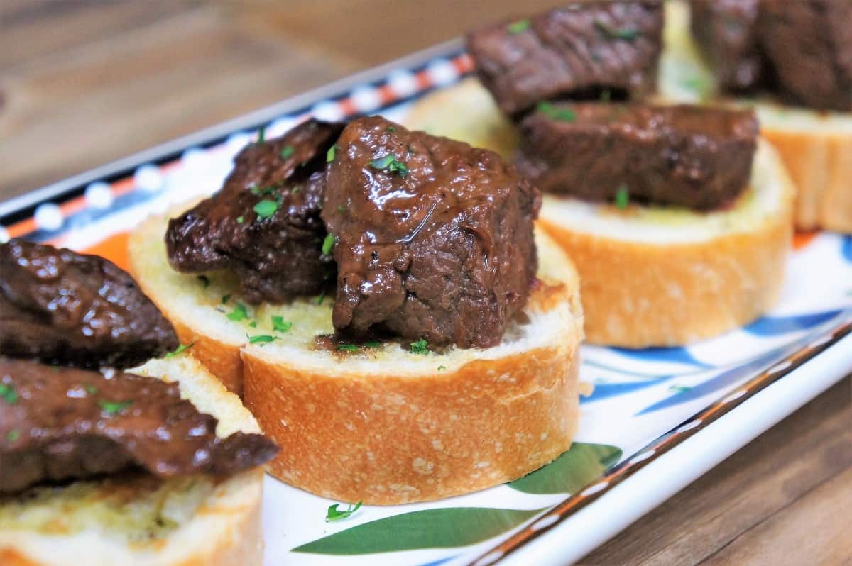 Cubes of sirloin steak on small toast rounds arranged on a colorful platter.