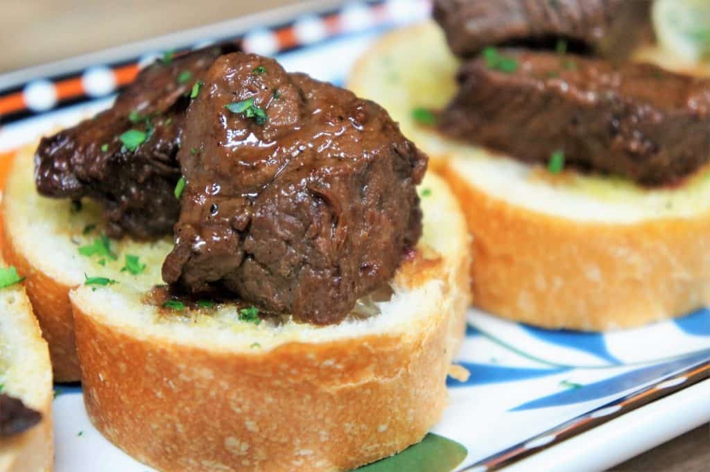 Cubes of sirloin steak on small toast rounds arranged on a colorful platter.