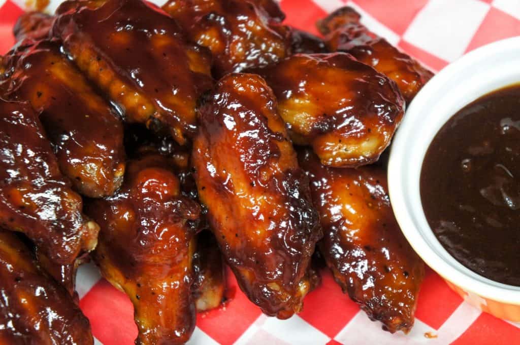Sticky chicken wings served on a red and white checkered liner and a side of barbecue sauce.