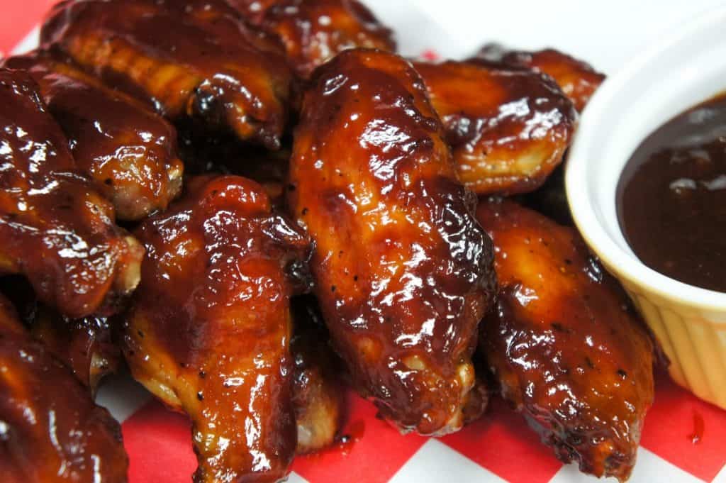 Sticky chicken wings served on a red and white checkered liner and a side of barbecue sauce.