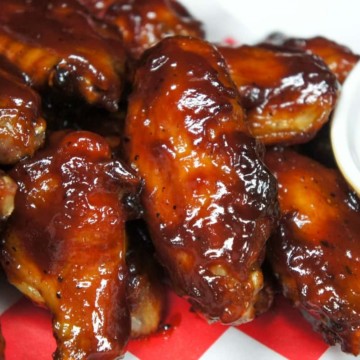 Sticky chicken wings served on a red and white checkered liner and a side of barbecue sauce.