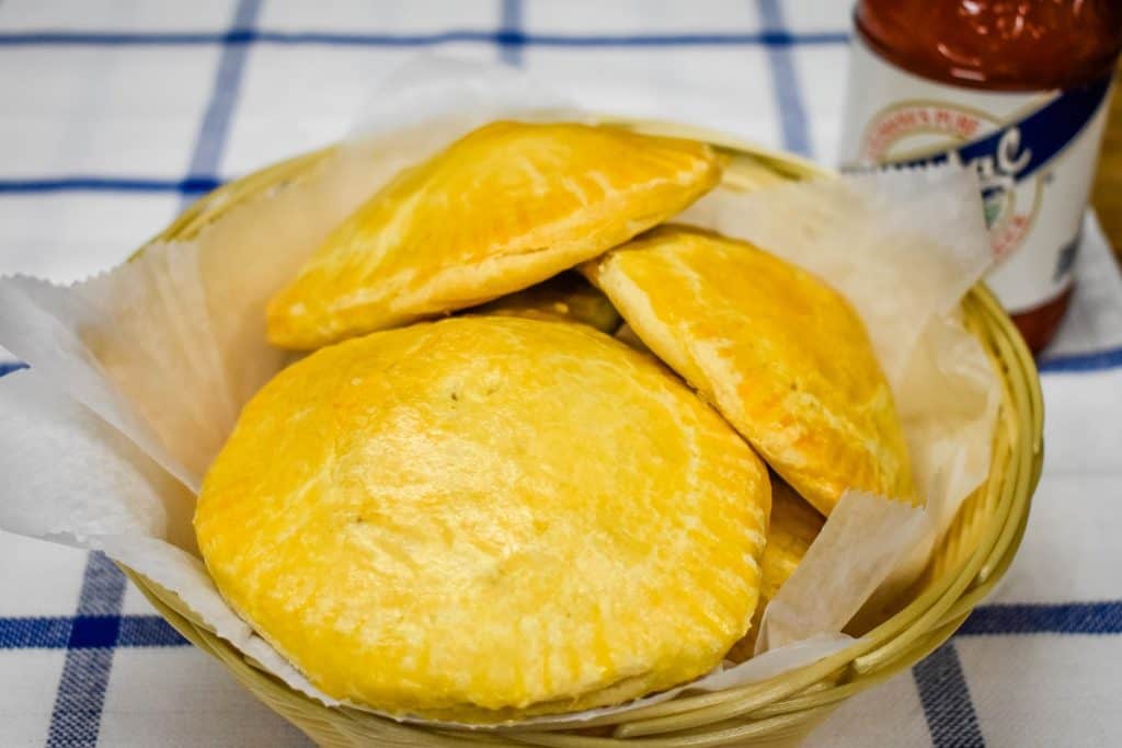 Baked stuffed biscuits arranged in a weaved basket with a bottle of hot sauce in the background.