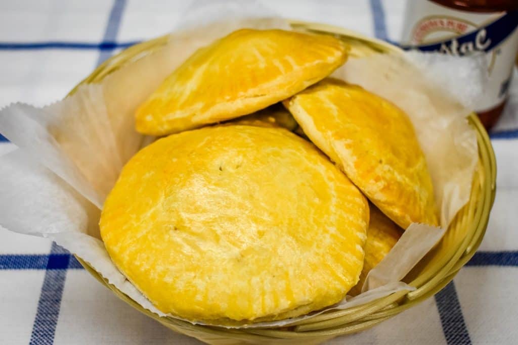 Baked stuffed biscuits in a weaved basket with a bottle of hot sauce in the background.