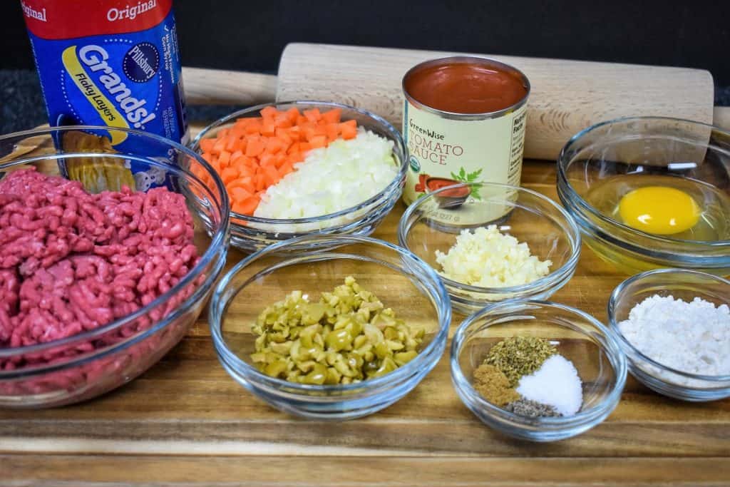 All the ingredients for these stuffed biscuits portioned out in glass bowls and arranged on a wood cutting board.