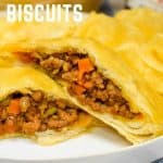 A baked biscuit stuffed with ground beef, cut in half and served on a white plate with potato chips.