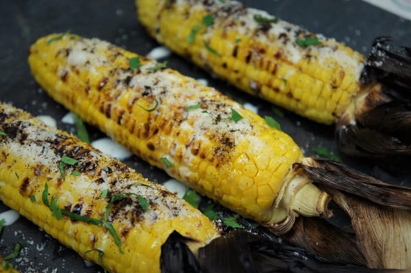 Grilled Corn served on slate board and topped with parmesan cheese, crema and chopped cilantro