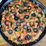 Taco Dip, refried beans and seasoned ground turkey topped with melted cheese, diced tomatoes, black olives and green onions served in a black bowl with corn tortilla chips and sour cream on the side.