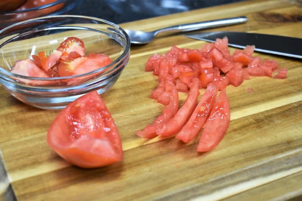 A tomato on a wood cutting board that has been seeded, cut into strips and diced.