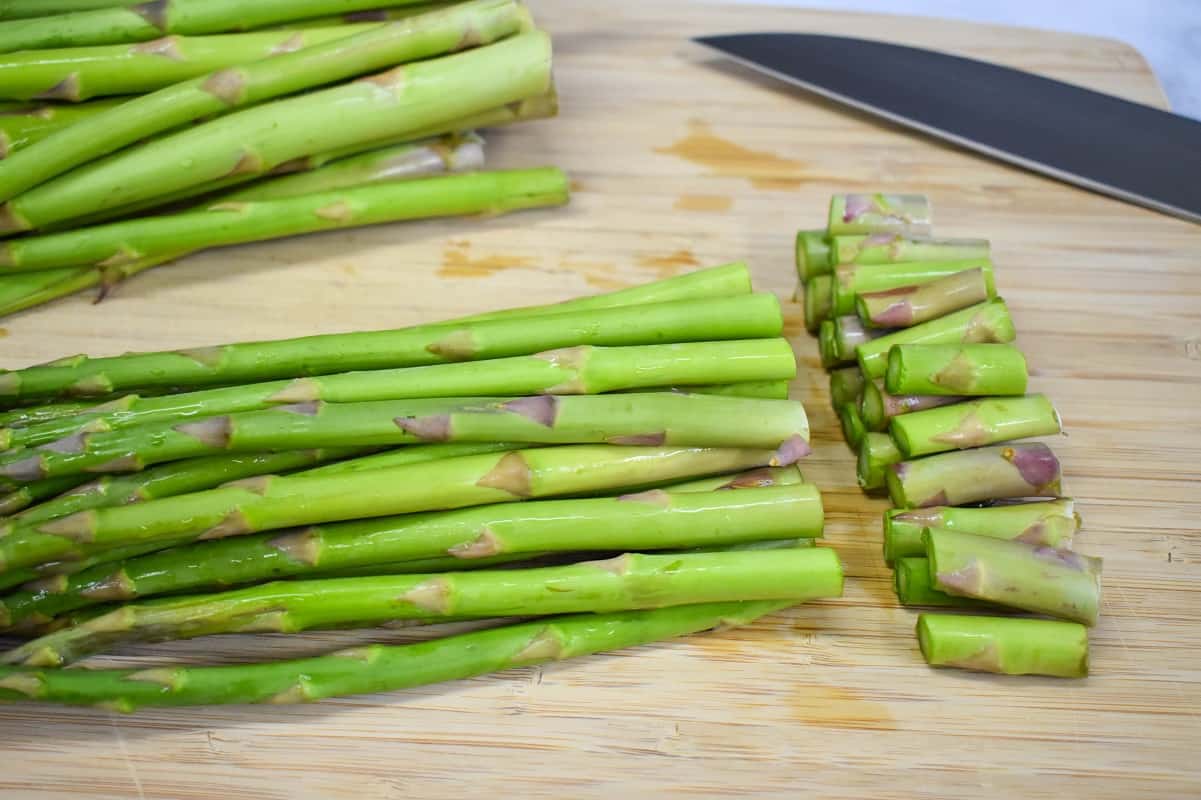 Asparagus spears with the woody ends trimmed off on a wood cutting board.