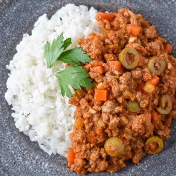 The picadillo served with white rice on the side on a gray plate and garnished with parsley leaves.